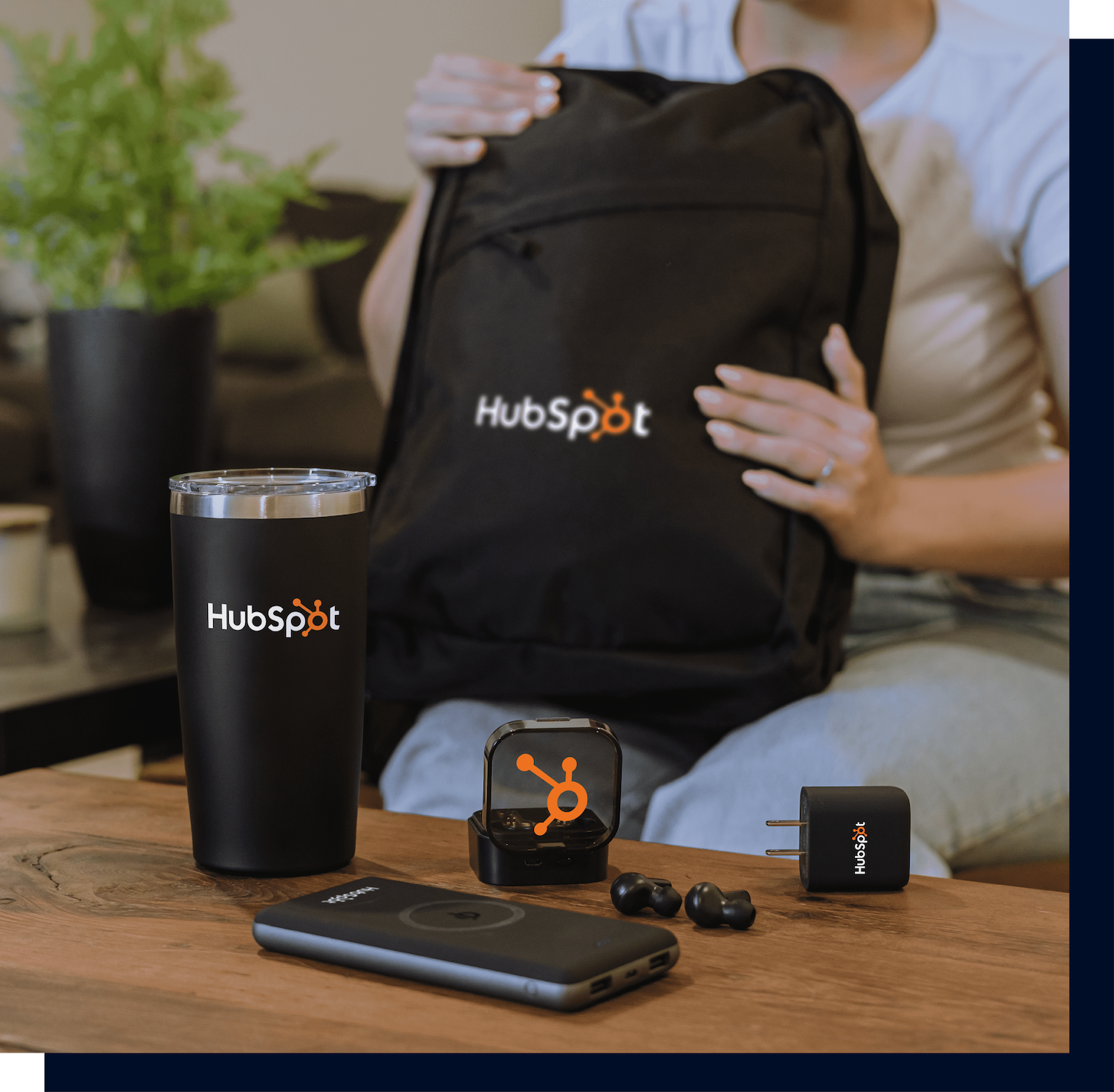 a table with differnet branded and promotional products on top and in the background there is an out of focus person holding a branded backpack